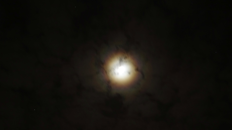 De maan met corona en iriserende wolken