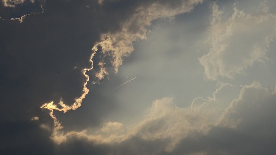 Wolken, een gat,  de zon en een vliegtuig