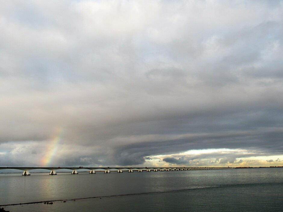 Bewolkt in de namiddag bij Colijnsplaat, regenboogje bij de Zeelandbrug, er is licht aan de horizon