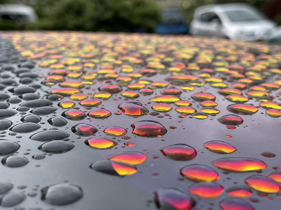 Kleurige regendruppels op auto dak in avondlicht