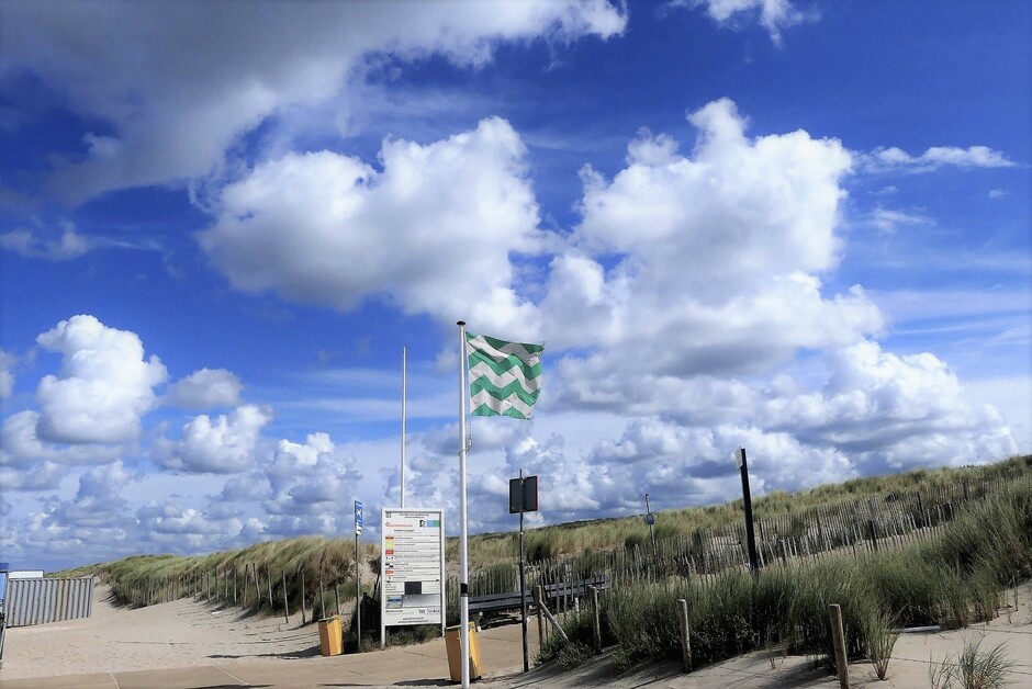 Zomerkoninkjes, druk strand met stapelwolken vlag zeewind