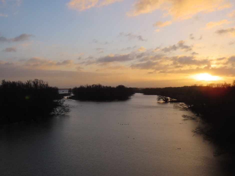 Vanaf de Tacitus brug, zonsopkomst met de uiterwaarden, en links de geul naar de rivier Waal.