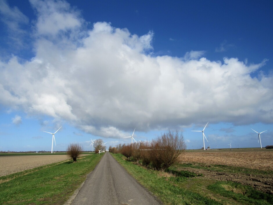 Flinke wolken die voorbij drijven, het is zonnig en er staat een koude, harde wind, de windmolens draaien hard, in de polder bij Kamperland