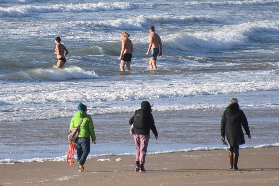 Warm aangekleed op het strand,toch zwemmers in zee