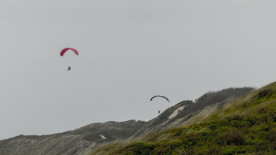 Paragliders zweven langs de duinen voor de regen valt